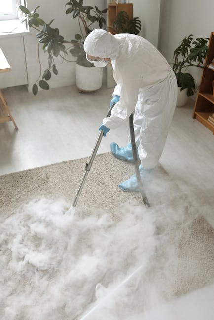A woman kneeling on a patterned rug in a living room, engaged in surface cleaning by wiping the wooden floor with a blue cloth. She is dressed in a light-colored striped shirt and jeans, with her hair